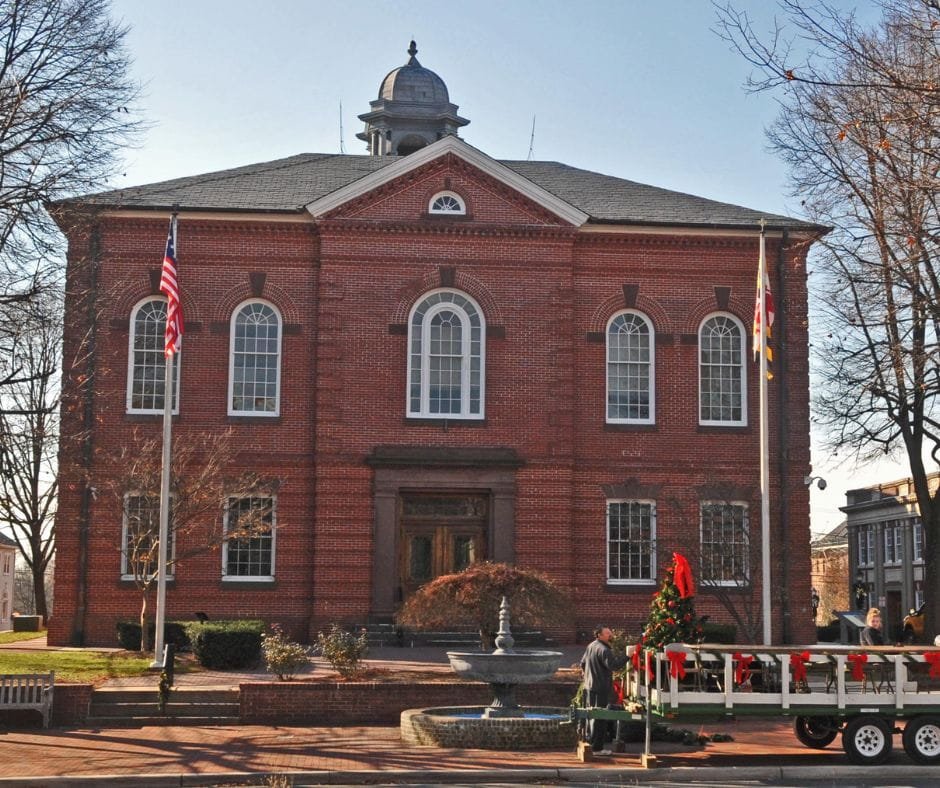 Historic Charles County courthouse building with red brick exterior, American and Maryland flags, and fountain in front