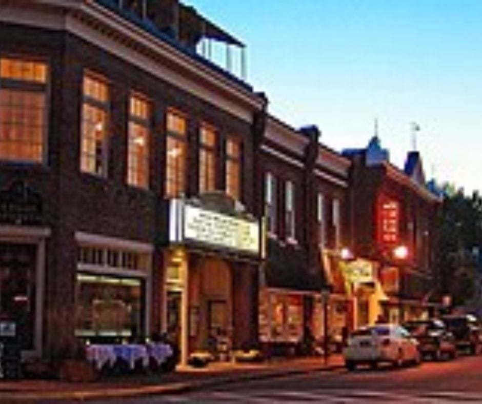 A cozy, lit up street in a historic downtown area at dusk with brick buildings and a theater marquee.