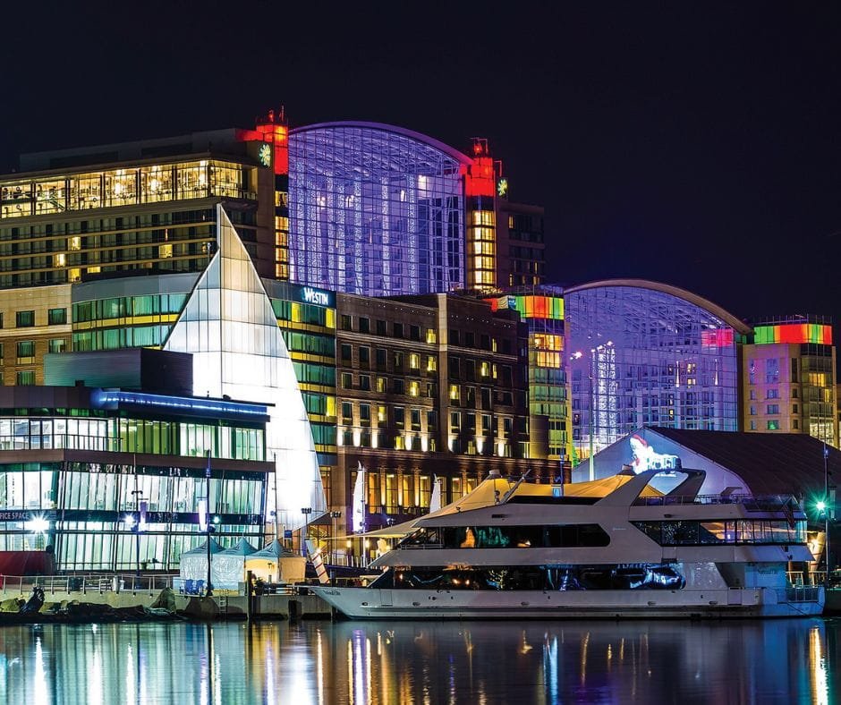 Night view of National Harbor waterfront with Gaylord National Resort and Westin hotel illuminated beside the marina.